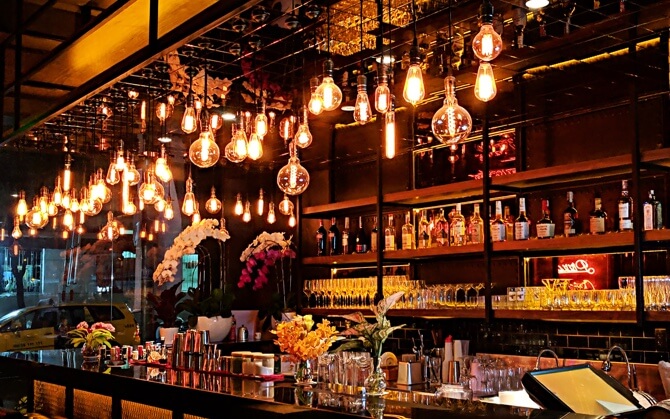 inside a cozy bar with lights hanging from the ceiling and glasses and bottles behind the bar